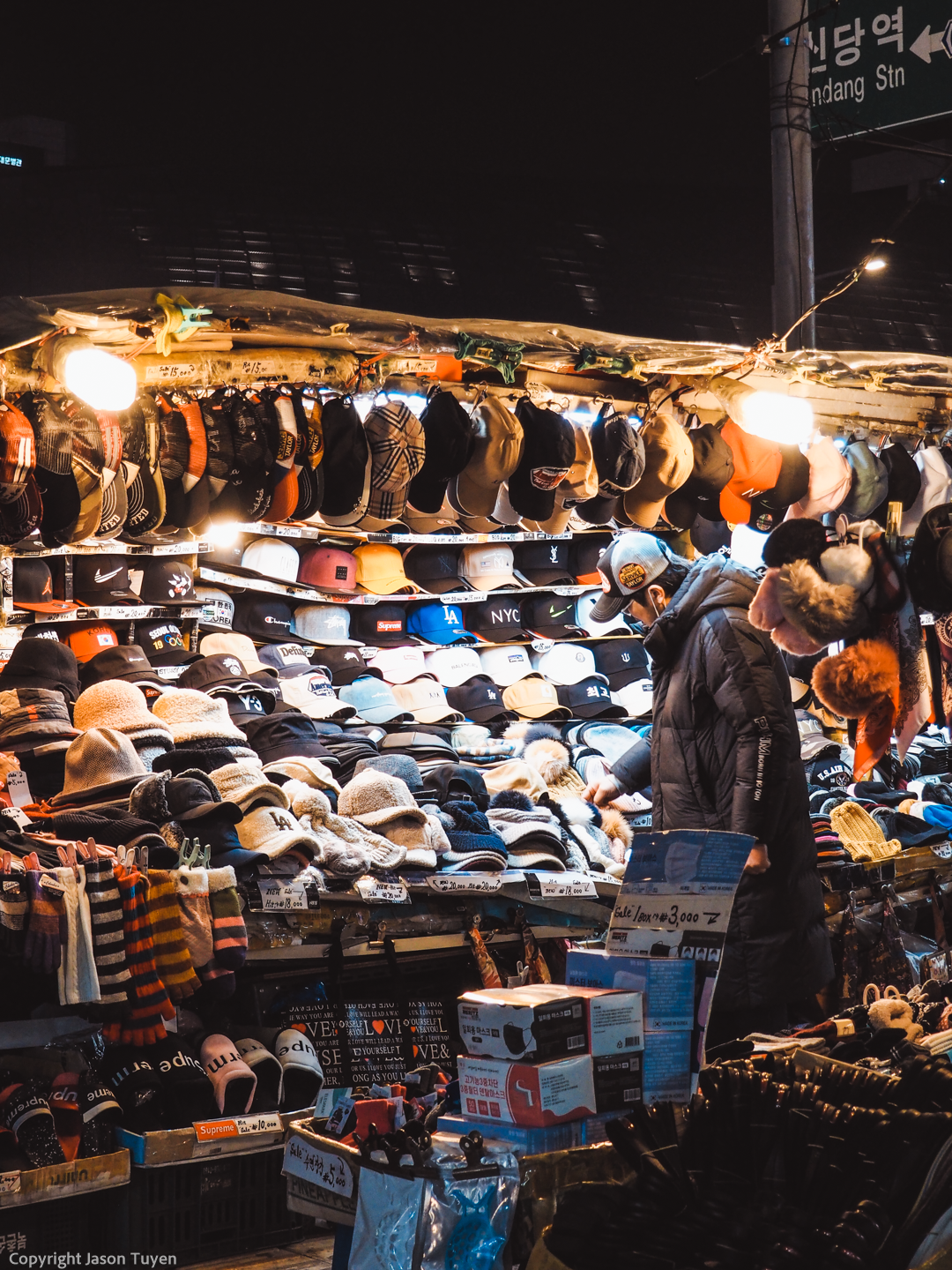 Older male looking at hats sold by South Korean street vendor.