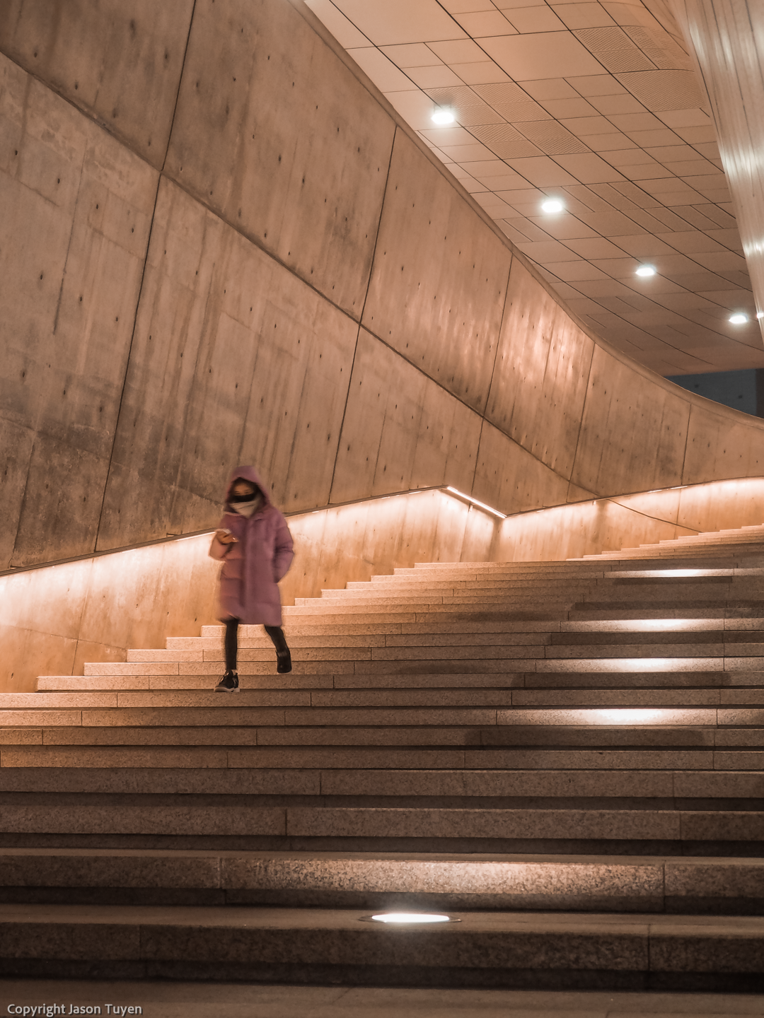 Woman in pink winter coat walks down stairs of the Dongdaemun Design Plaza.