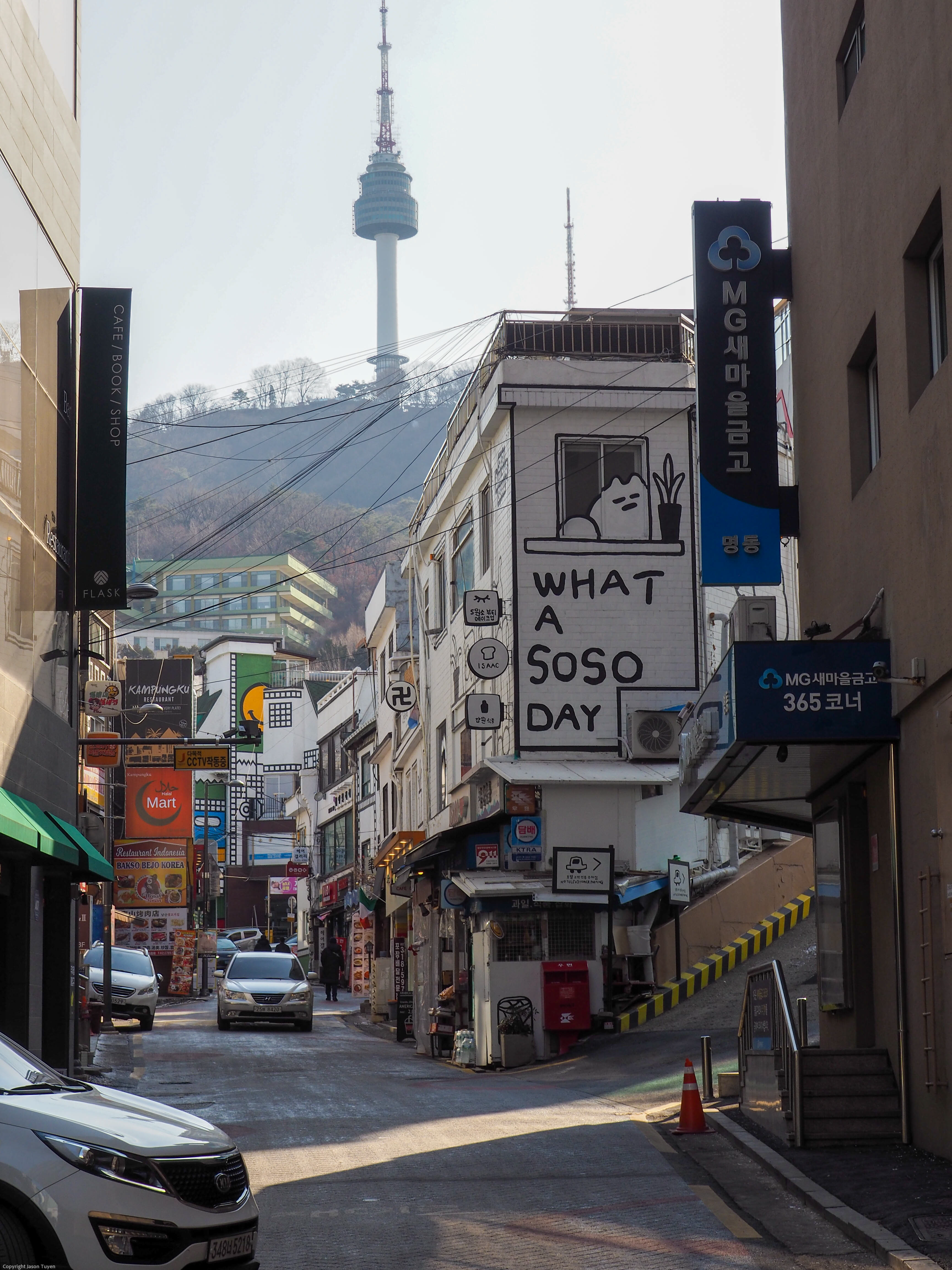 The N Seoul Tower as seen from the base of a busy alleyway during midday.